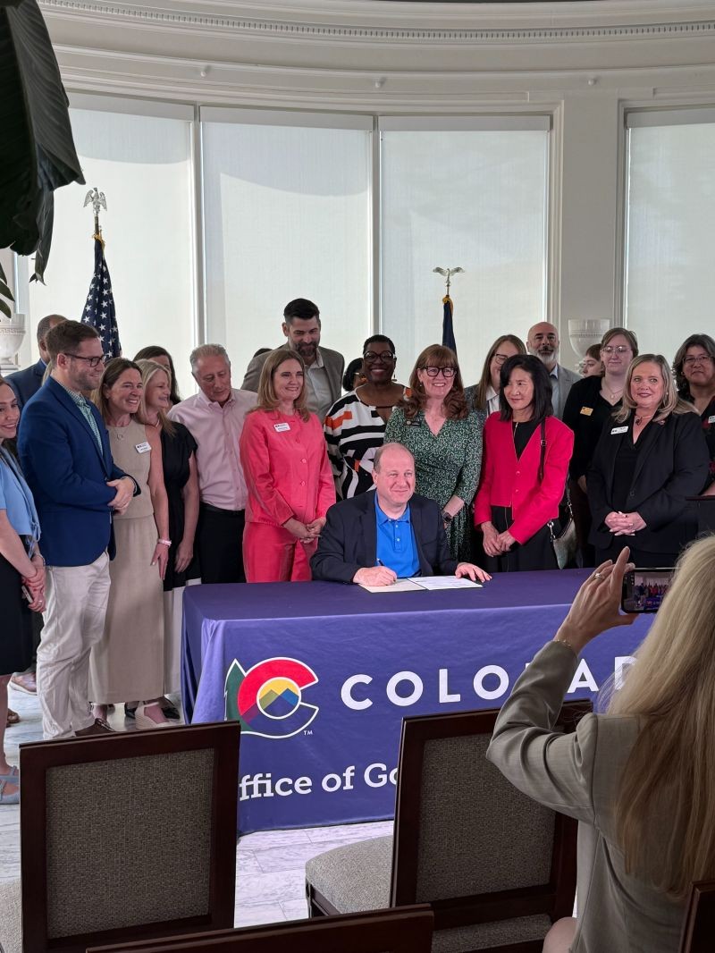 Man signs a bill group of supporters behind pose for a picture.