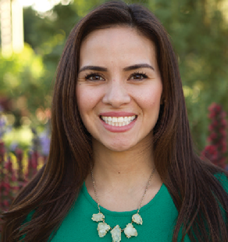 Woman with long brown hear smiling in a green shirt with a chunky necklace