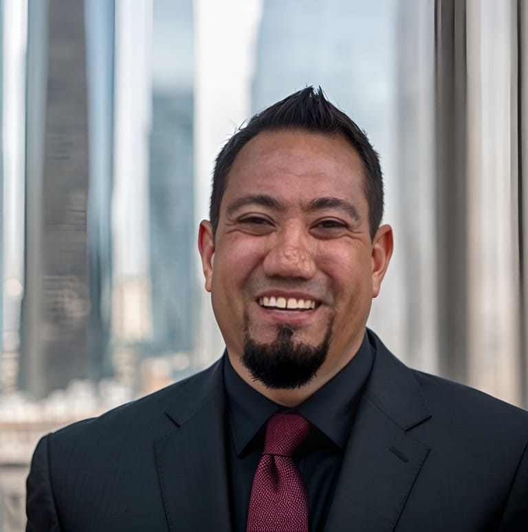 Man with a goatee smiling in a black suit and tie